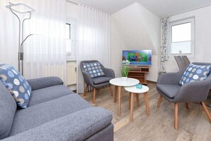 A modern living room with grey sofas, a round coffee table, and a flat-screen TV. - Holiday apartments "Robbe" (Esens-Bensersiel)