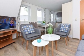 A living room with a television, two grey armchairs with polka dot cushions, a white coffee table, and a small plant. - Holiday apartments "Robbe" (Esens-Bensersiel)