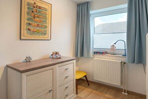 A child's room with a dresser, a window with curtains, a radiator, and a teddy bear on the dresser. - Holiday apartment with 1 bedroom (Greetsiel)
