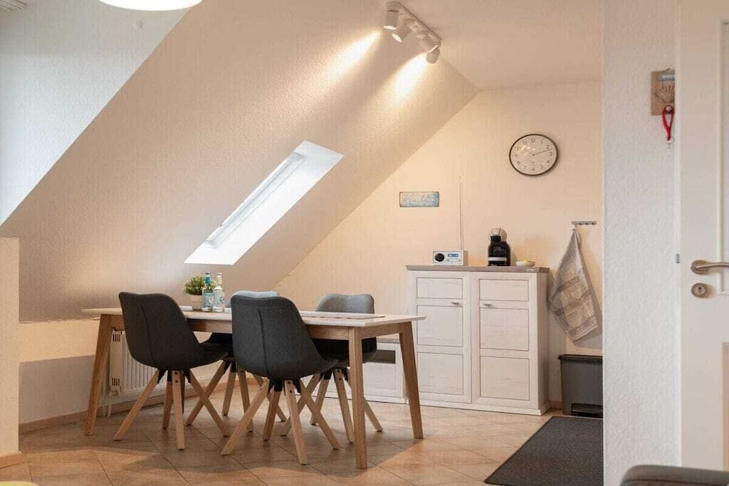 Un coin repas avec une table et des chaises, une horloge au mur et une fenêtre.