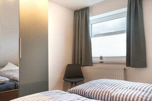 Une chambre avec deux lits, une chaise, une fenêtre avec des rideaux et un radiateur.
