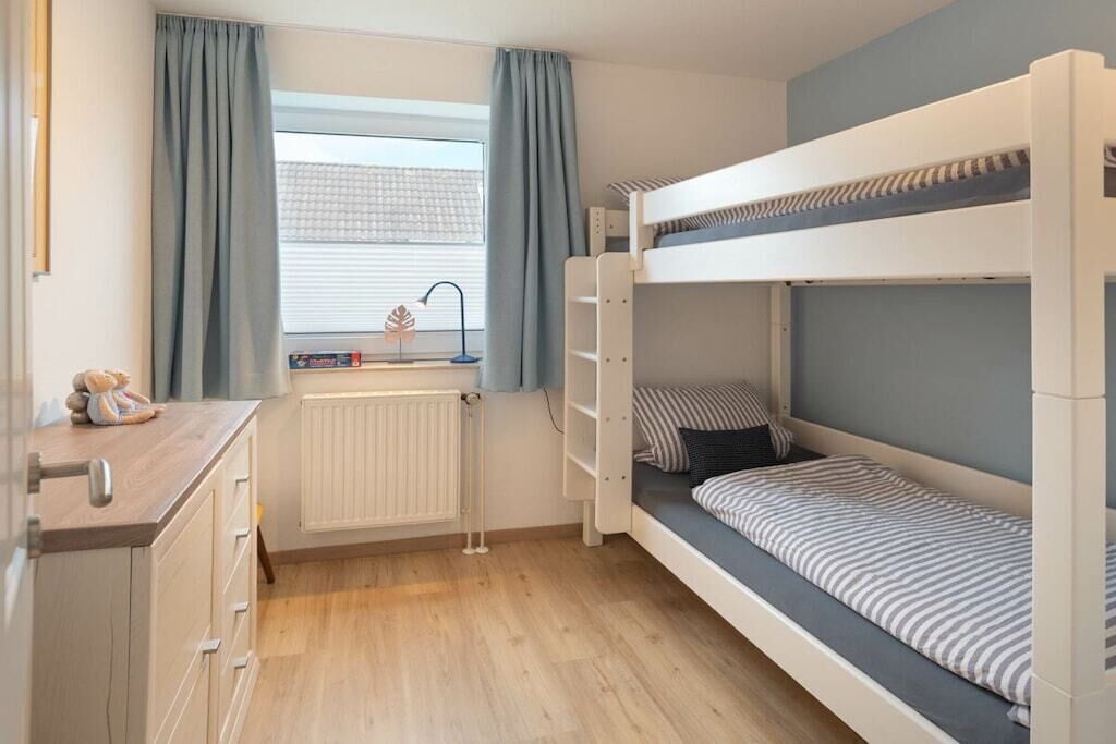 A bunk bed room with a window, radiator, and a desk with drawers.
