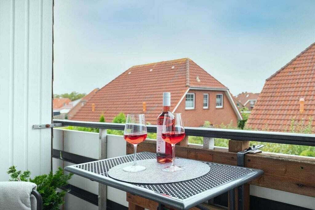 Un balcon avec une table, deux verres de vin rouge et une bouteille posée sur une table en métal.