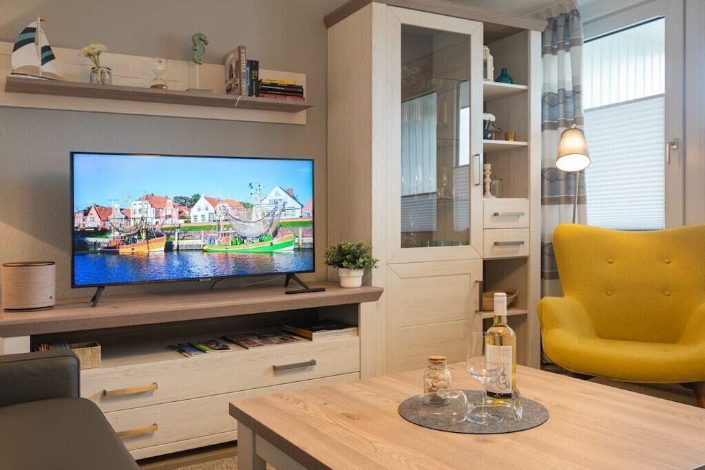 Una sala de estar moderna con un televisor de pantalla plana, muebles de madera, un sillón amarillo y un aparador de vidrio.