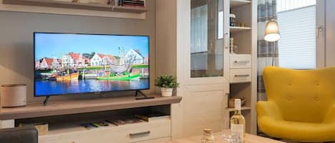 A modern living room with a flat-screen TV, wooden furniture, a yellow armchair, and a glass cabinet.