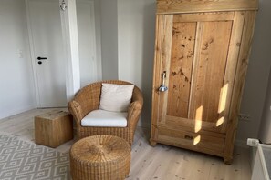 A room with a wicker chair, a small ottoman, a wooden cabinet, and a white door. - Holiday home with 4 bedrooms (Galmsbüll)