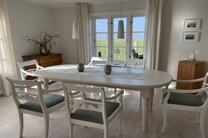 Un coin repas avec une table et des chaises blanches, une vue sur l’extérieur et un buffet en bois.