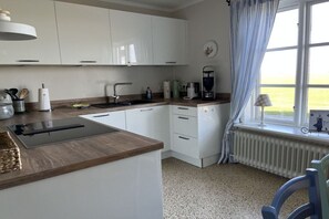 Eine Küche mit weißen Schränken, einer Kaffeemaschine und einem Fenster mit Vorhängen.