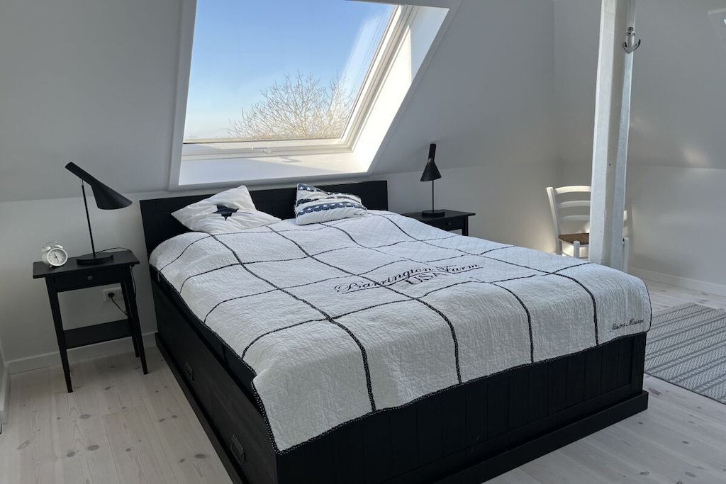 Ein Schlafzimmer mit Oberlicht, einem Bett mit Tagesdecke, Nachttischen mit Lampen und einem Sessel.