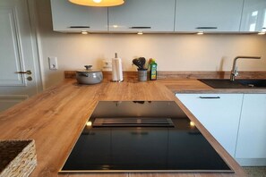 A modern kitchen with a built-in stove, wooden countertop, and white cabinets. - Holiday home with 4 bedrooms (Galmsbüll)