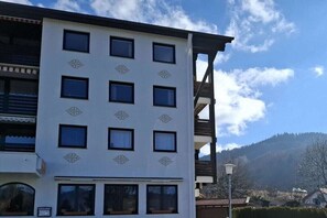 Ein mehrstöckiges Gebäude mit weißer Fassade und einem Balkon auf der rechten Seite.