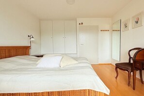 A bedroom with a large bed, a wooden headboard, a bedside lamp, a wardrobe, a chair, and a mirror on the wall. - Floor cutting suites "Wanderlust" (Tegernsee)
