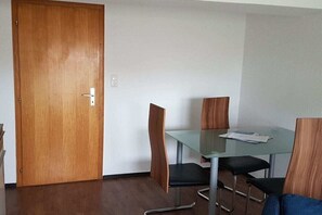 A room with a wooden door, a glass table with chairs, and a white wall. - Holiday apartment with 1 bedroom (Dornumersiel)