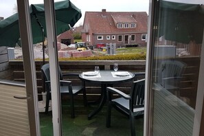 An outdoor patio with a table set for two, surrounded by chairs, and a view of a residential area with houses and a construction vehicle in the background. - Holiday apartment with 1 bedroom (Dornumersiel)