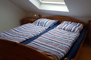 A single bed with a wooden frame and a slatted headboard, a bedside table with a lamp, and a skylight above. - Holiday apartment with 1 bedroom (Dornumersiel)