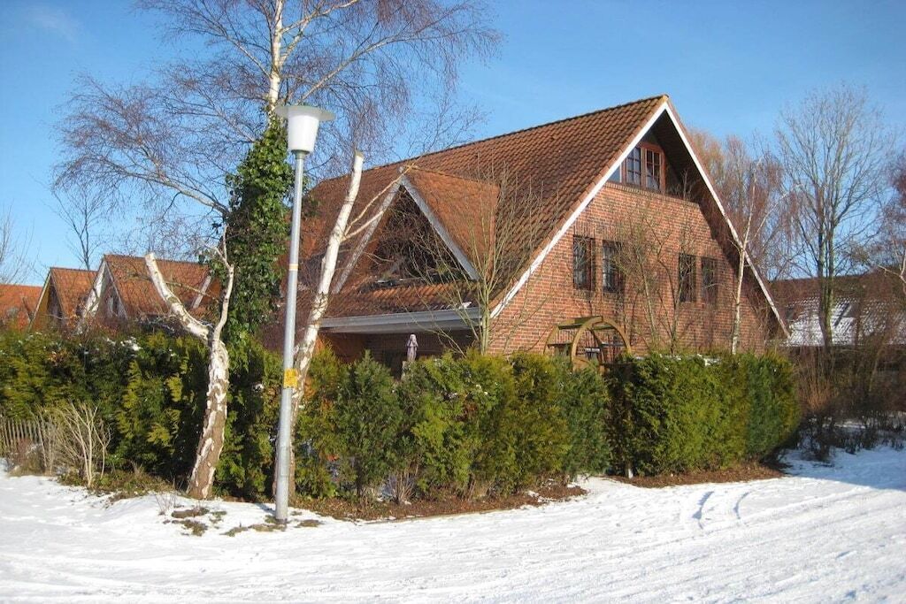 Une maison en briques avec un toit en pente, entourée d’un paysage enneigé et d’arbres sans feuilles.