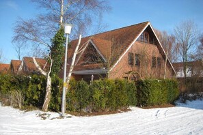 Ein Backsteinhaus mit geneigtem Dach, umgeben von schneebedecktem Boden und kahl stehenden Bäumen.