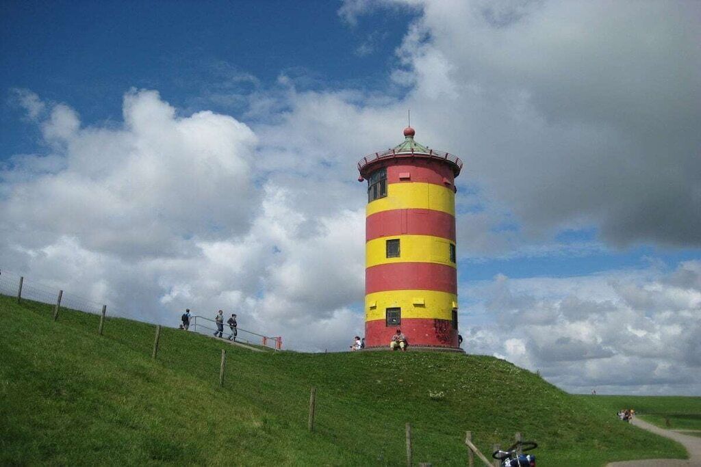Ein Leuchtturm mit rot-gelben Streifen steht auf einem grasbewachsenen Hügel unter blauem Himmel.