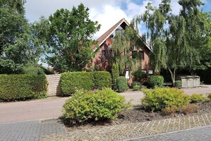 A brick house with a sloped roof, surrounded by well-maintained hedges and trees. - Holiday apartment with 1 bedroom (Krummhörn-Greetsiel)