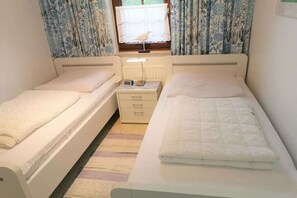 Ein Zimmer mit zwei Einzelbetten, einem Nachttisch mit Lampe und einem Fenster mit Vorhängen.