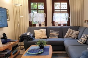 A living room with a sofa, a coffee table, a TV, and a bookshelf. - Holiday apartment with 1 bedroom (Krummhörn-Greetsiel)