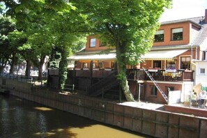 A riverside building with a balcony, a staircase, and a view of the water. - Holiday apartment with 1 bedroom (Krummhörn-Greetsiel)