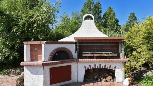 Un forno a mattoni all'aperto con un camino, immerso nel verde.