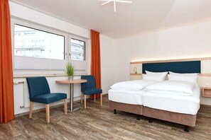 A hotel room with a bed, two chairs, a small table, a window with curtains, and a radiator. - Holiday apartments "Seagull 2" (Esens-Bensersiel)