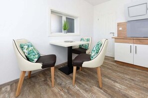 A small kitchen with a dining table and two chairs, a window with a plant, and a white cabinet. - Holiday apartments "Seagull 2" (Esens-Bensersiel)