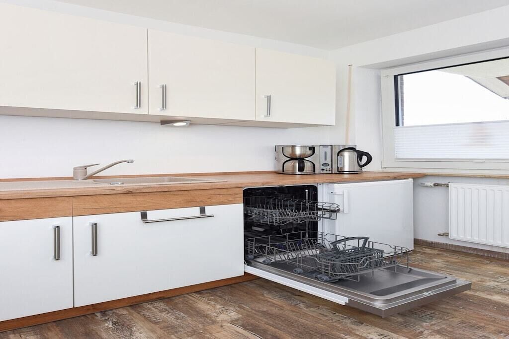 A modern kitchen with white cabinets, a wooden countertop, and a dishwasher.