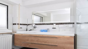 Un bagno moderno con un lavandino bianco, un mobile contenitore in legno, uno specchio e un tappeto blu.