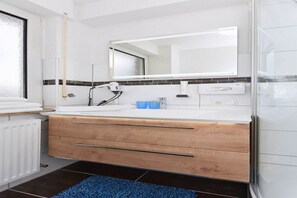 Ein modernes Badezimmer mit einem weißen Waschbecken, einer Holzkommode, einem Spiegel und einem blauen Teppich.