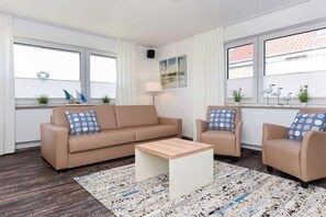 Ein Wohnzimmer mit einem beigen Sofa, zwei Sesseln, einem Couchtisch und einem gemusterten Teppich.