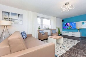 A modern living room with a sofa, armchairs, a coffee table, and a TV. - Holiday apartments "Seagull 2" (Esens-Bensersiel)
