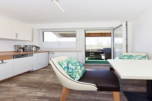 A modern kitchen with white cabinets, a wooden countertop, and a dining area with a white table and a cushioned chair. - Holiday apartments "Seagull 2" (Esens-Bensersiel)