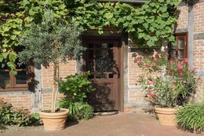 Un bâtiment en briques avec une porte en bois, des plantes en pot et un mur recouvert de lierre.