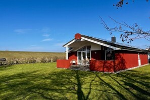 A red building with a satellite dish, a glass door entrance, and a lawn in front. - Holiday home with 3 bedrooms (Wesselburenerkoog)