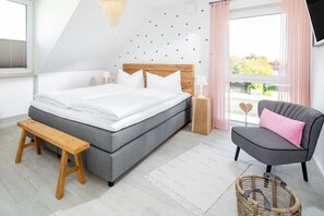 Een slaapkamer met een bed, een bankje, een stoel, een nachtkastje en een raam met gordijnen.