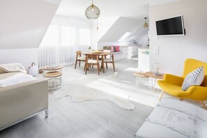 A modern apartment with a dining area, a sofa, a yellow armchair, and a TV mounted on the wall. - Holiday apartment with 1 bedroom (Norddeich)
