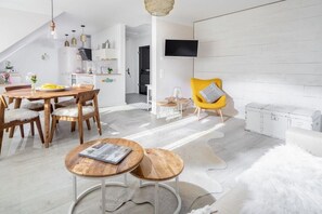 A modern living space with a dining area, a yellow armchair, and a television mounted on the wall. - Holiday apartment with 1 bedroom (Norddeich)