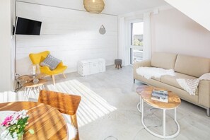 Ein modernes Wohnzimmer mit einer Couch, einem gelben Sessel, einem Couchtisch und einem an der Wand befestigten Fernseher.