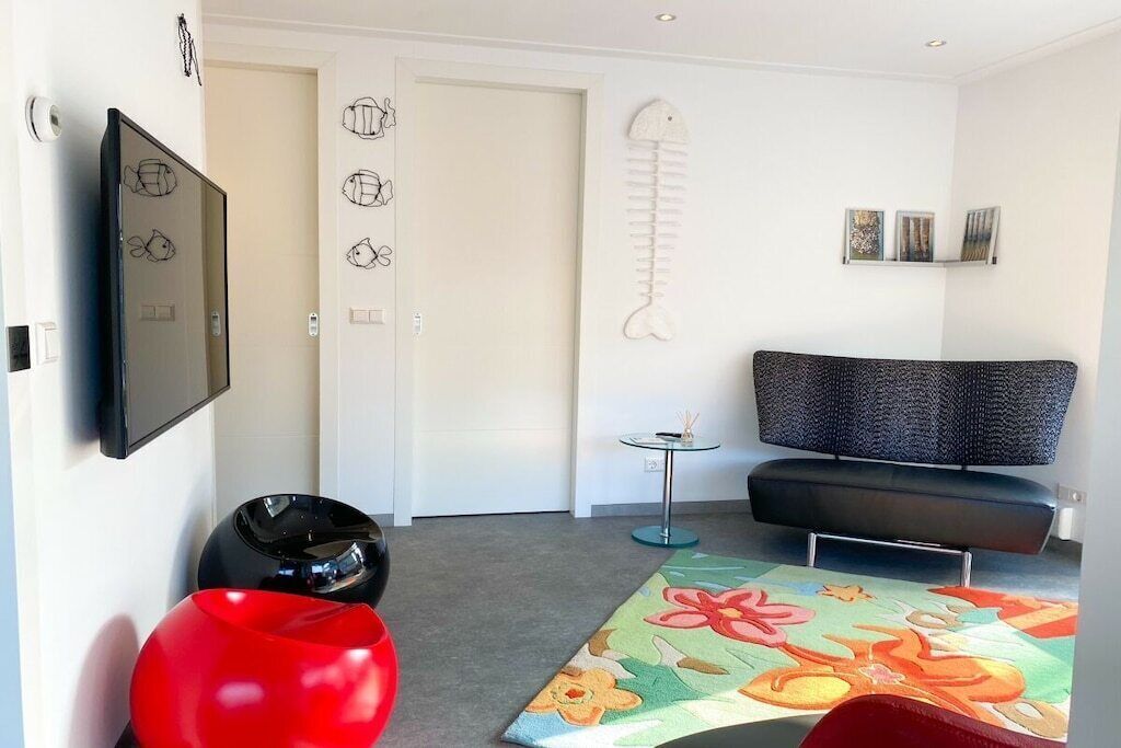 A modern living room with a sofa, a television, a fish sculpture, and a colorful rug.