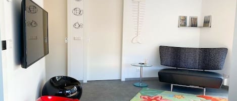 A modern living room with a sofa, a television, a fish sculpture, and a colorful rug.