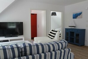 A living room with a television on a white stand, a striped sofa, a blue cabinet, and a red door in the background. - Holiday apartment with 1 bedroom (Koserow)