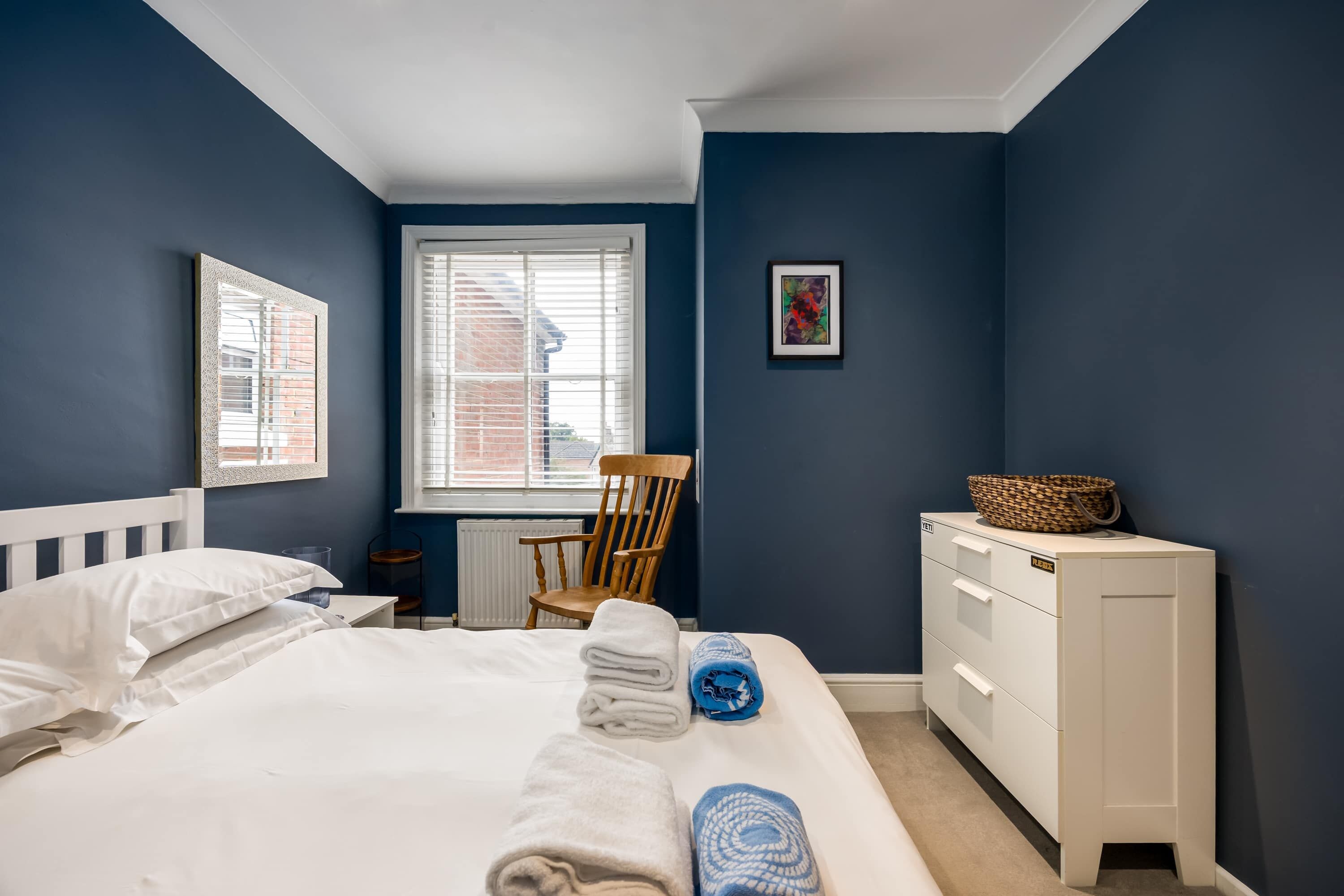 A bedroom with a bed, a chair, a dresser, and a window.
