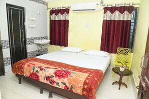 A bedroom with a bed, a bedside table with a plant, a window with curtains, and a bathroom with a sink and mirror. - Sai Shakti Guest House (Bhubaneswar)