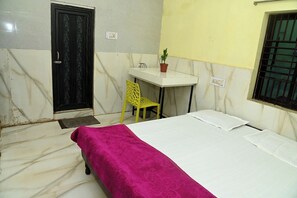 A room with a bed, a desk, a chair, a potted plant, and a window with bars. - Sai Shakti Guest House (Bhubaneswar)