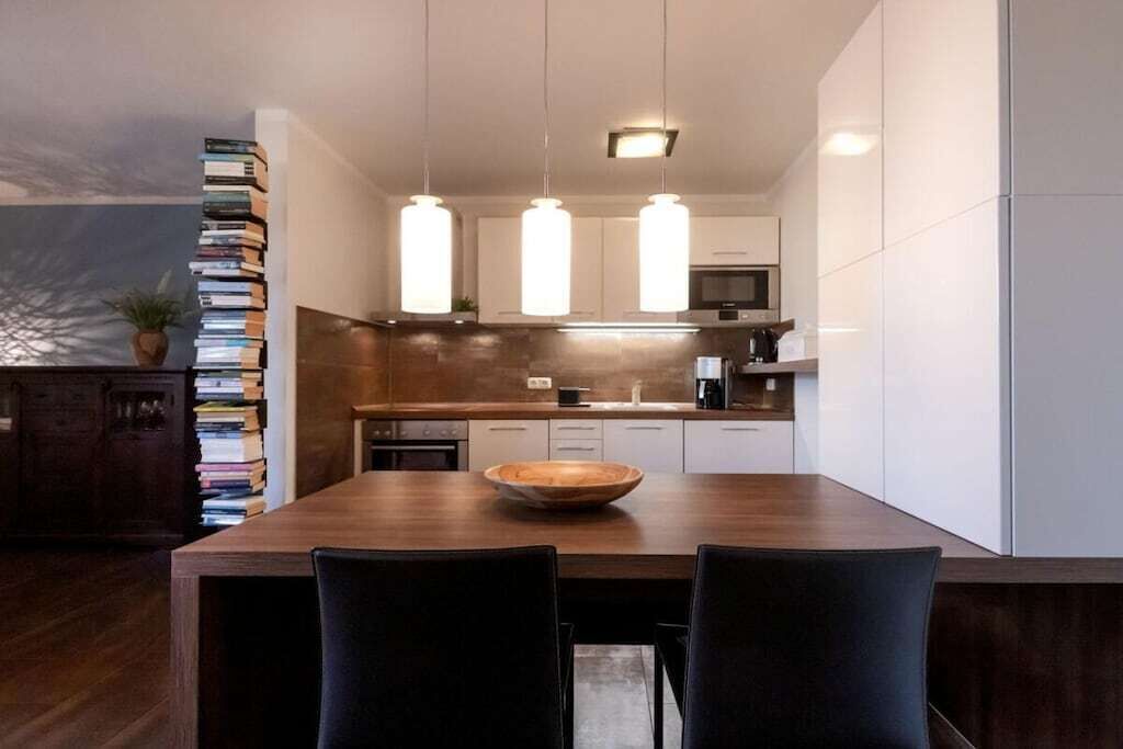 Une cuisine moderne avec une table à manger en bois, des luminaires suspendus et des meubles de rangement blancs.