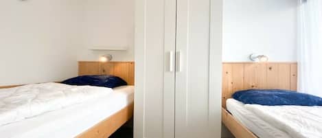 A bedroom with two single beds, a white wardrobe, wooden headboards, and a wall-mounted light fixture.