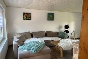 A modern living room with a sectional sofa, a small wooden table, and two wall-mounted lamps. - Holiday home in the Harz Mountains with 2 bedrooms (Harzgerode OT Güntersberge)